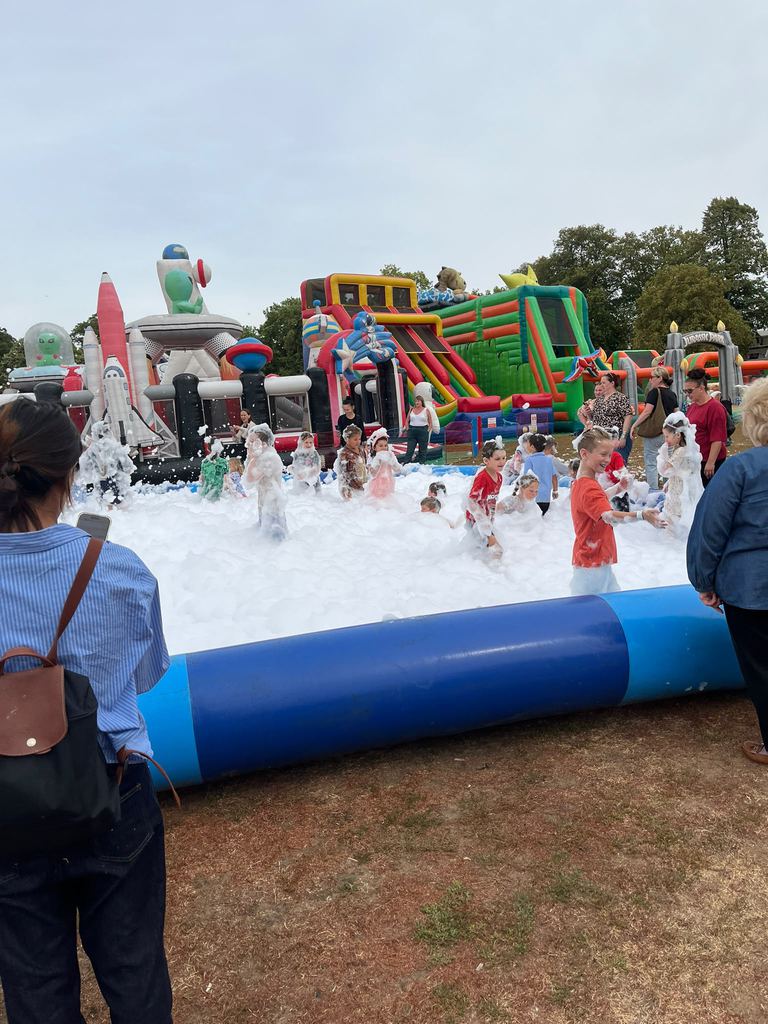 Children playing in deep white foam in a foam pit at a busy outdoor fun day