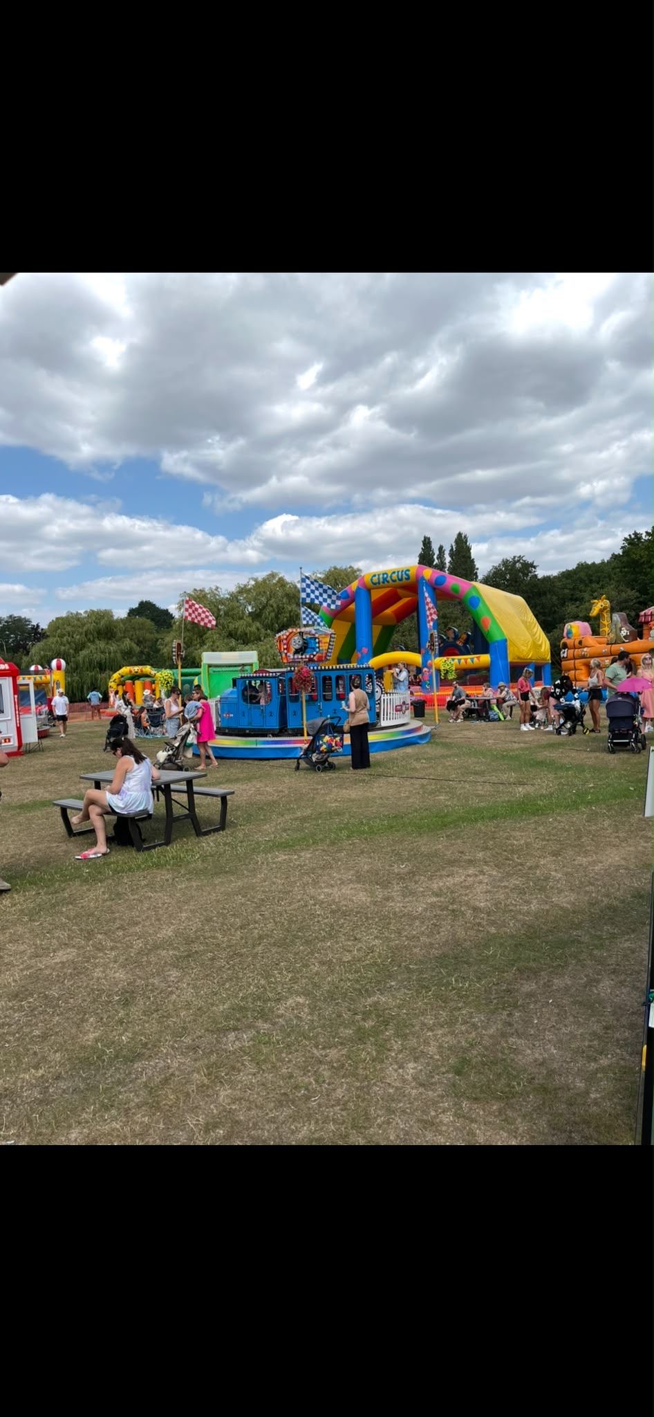 Families at a picnic table beside a circus inflatable and a kids' train ride at a community event
