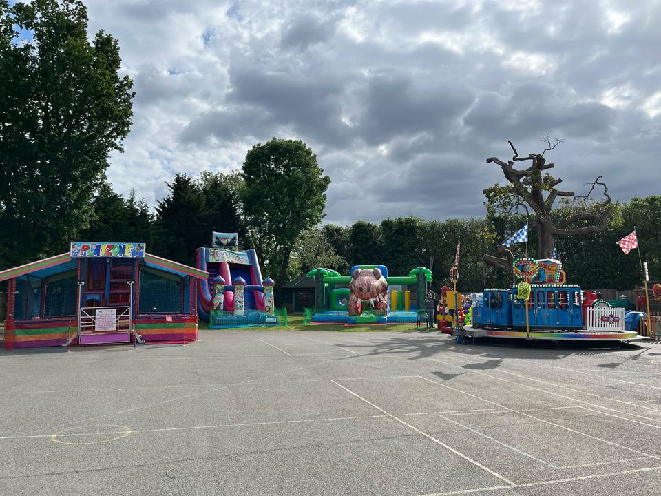 A wide view of a school fun day with soft play, a slide and a train ride