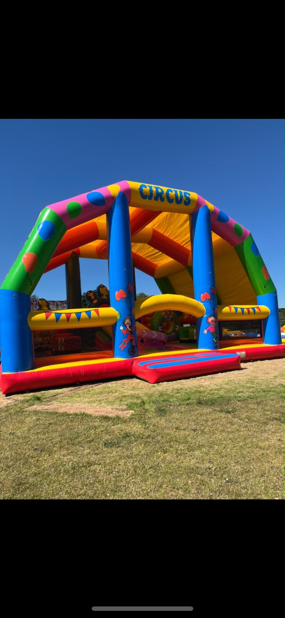 A large circus-themed inflatable arch and bounce area decorated with balloons and clowns