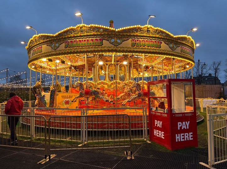 A traditional illuminated carousel with hand-painted gallopers, lit up at dusk