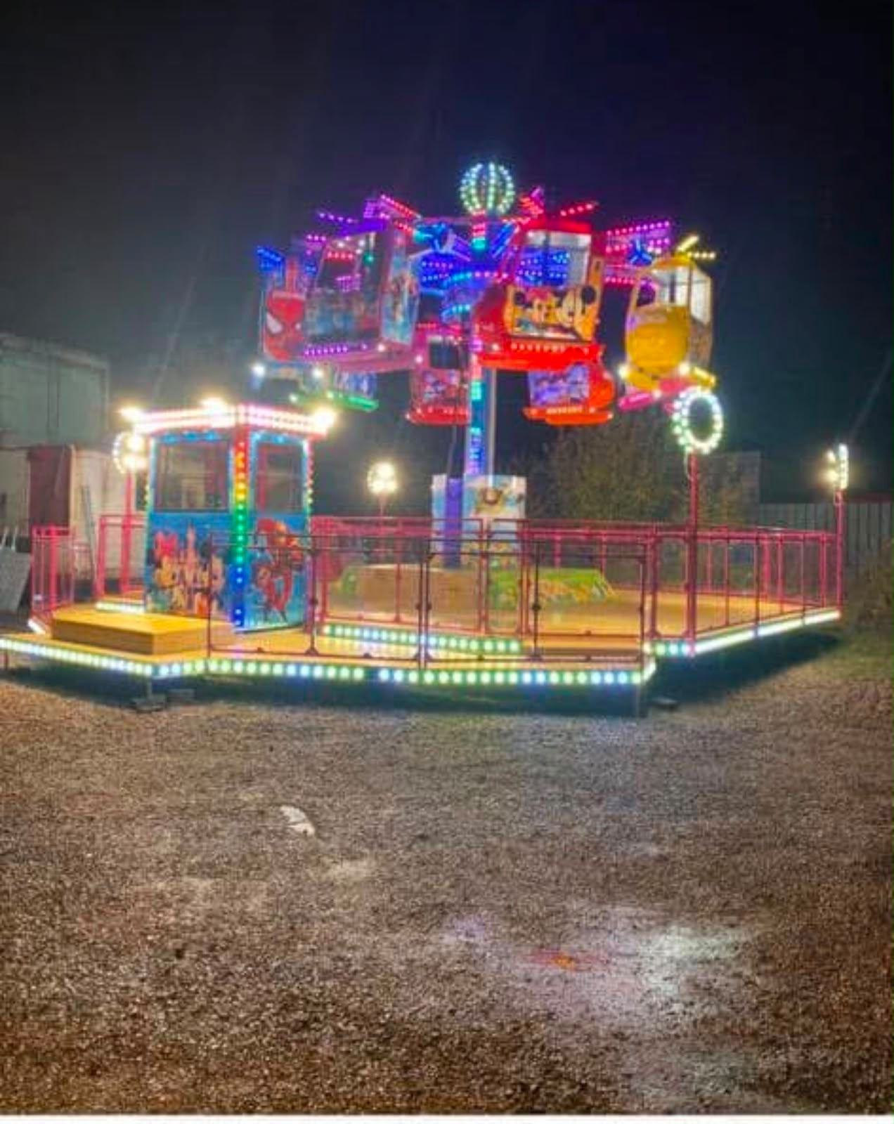 A kids' helicopter ride lit up at night, with helicopter and character cars on spinning arms